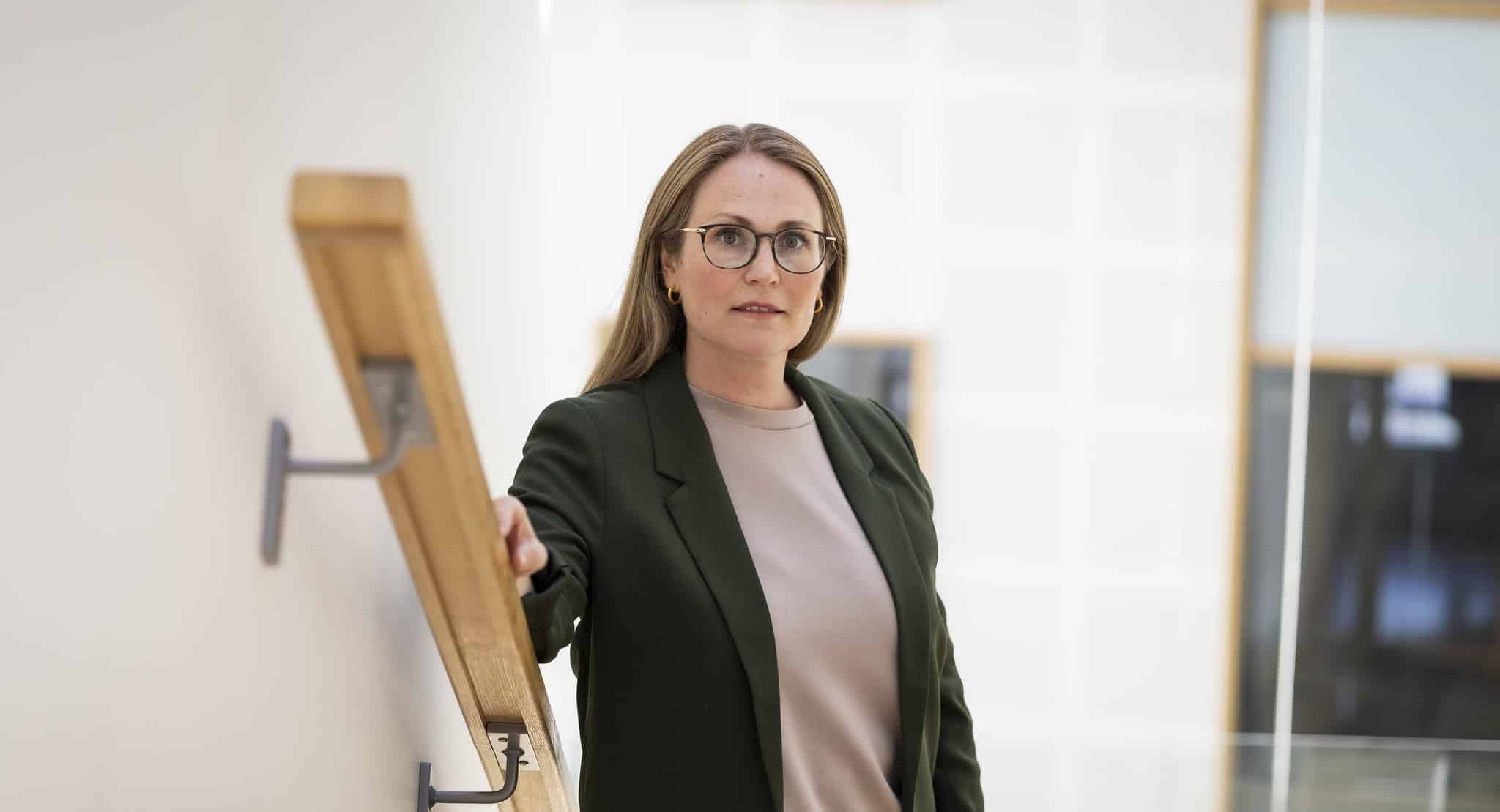 Bilde av Lene Knapstad. Dame i gr&oslash;n dressjakke og lys gensar. St&aring;r i trappa og ser alvorleg i kamera.